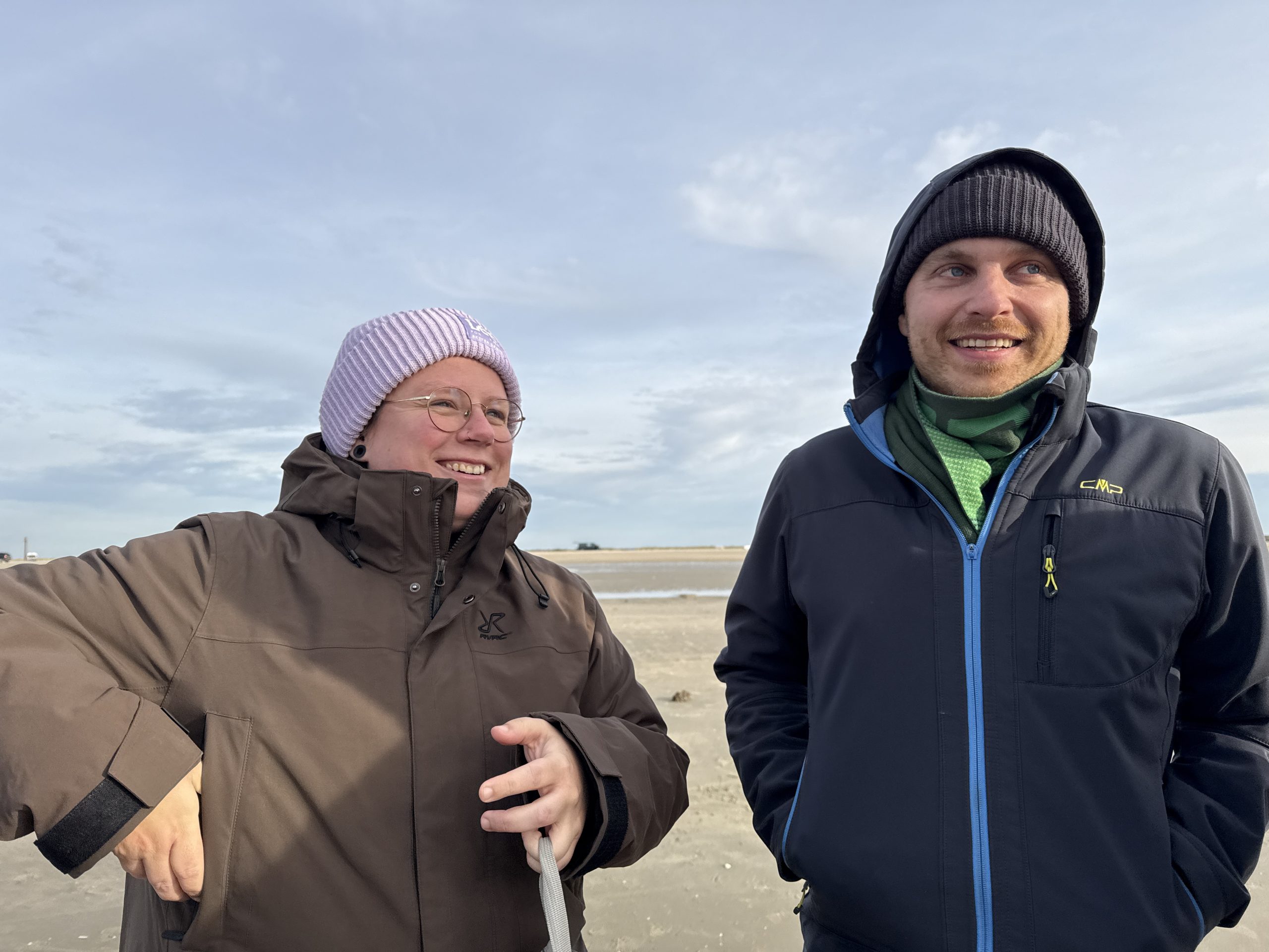 zwei fröhliche Menschen am Strand in warmer Bekleidung
